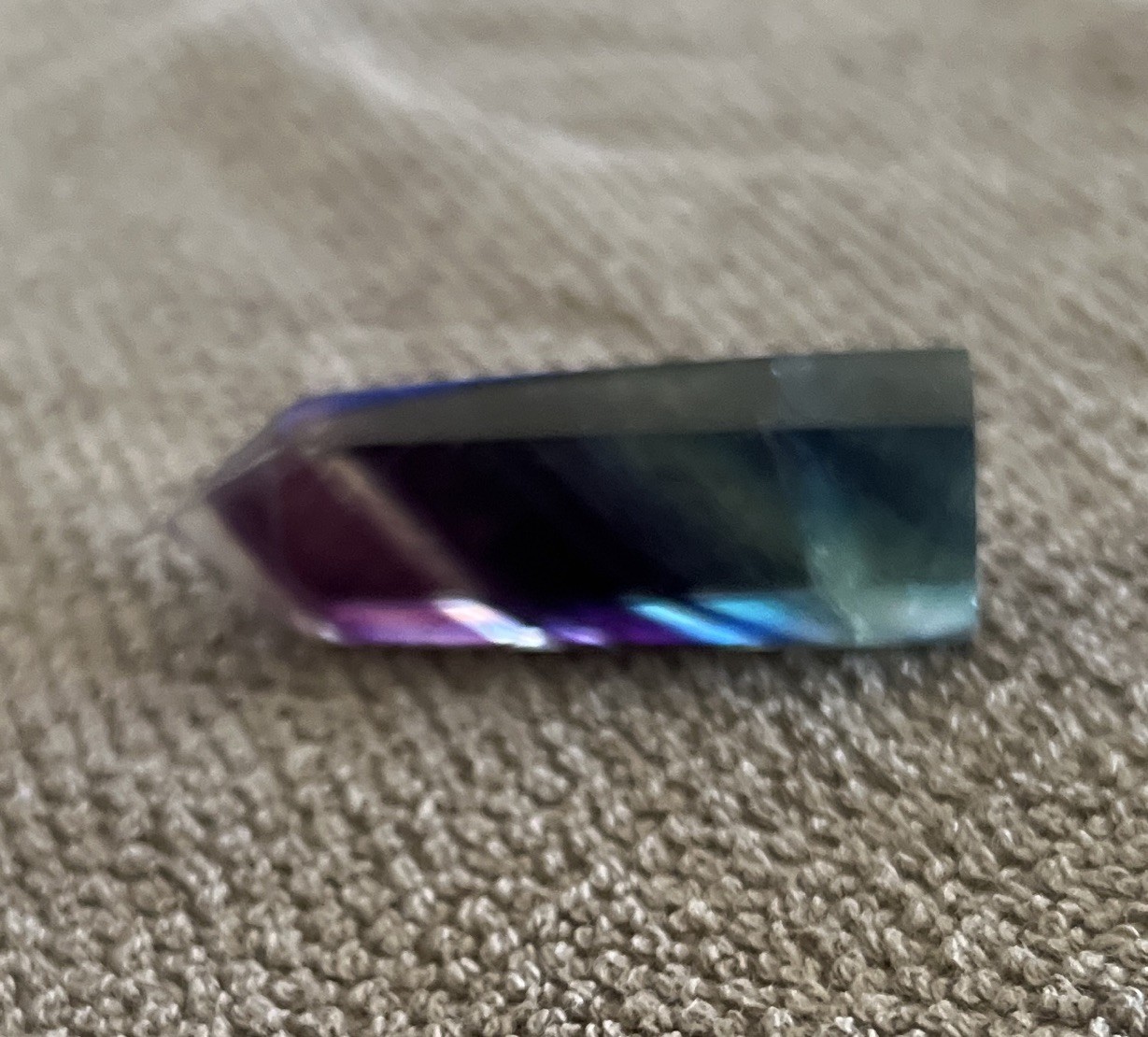 A polished rainbow fluorite crystal wand featuring distinct purple,blue,green