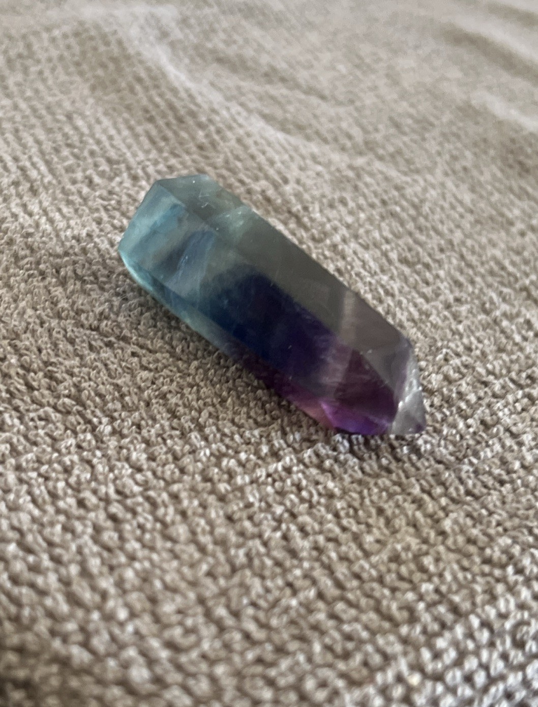 A polished rainbow fluorite crystal wand featuring distinct purple,blue,green