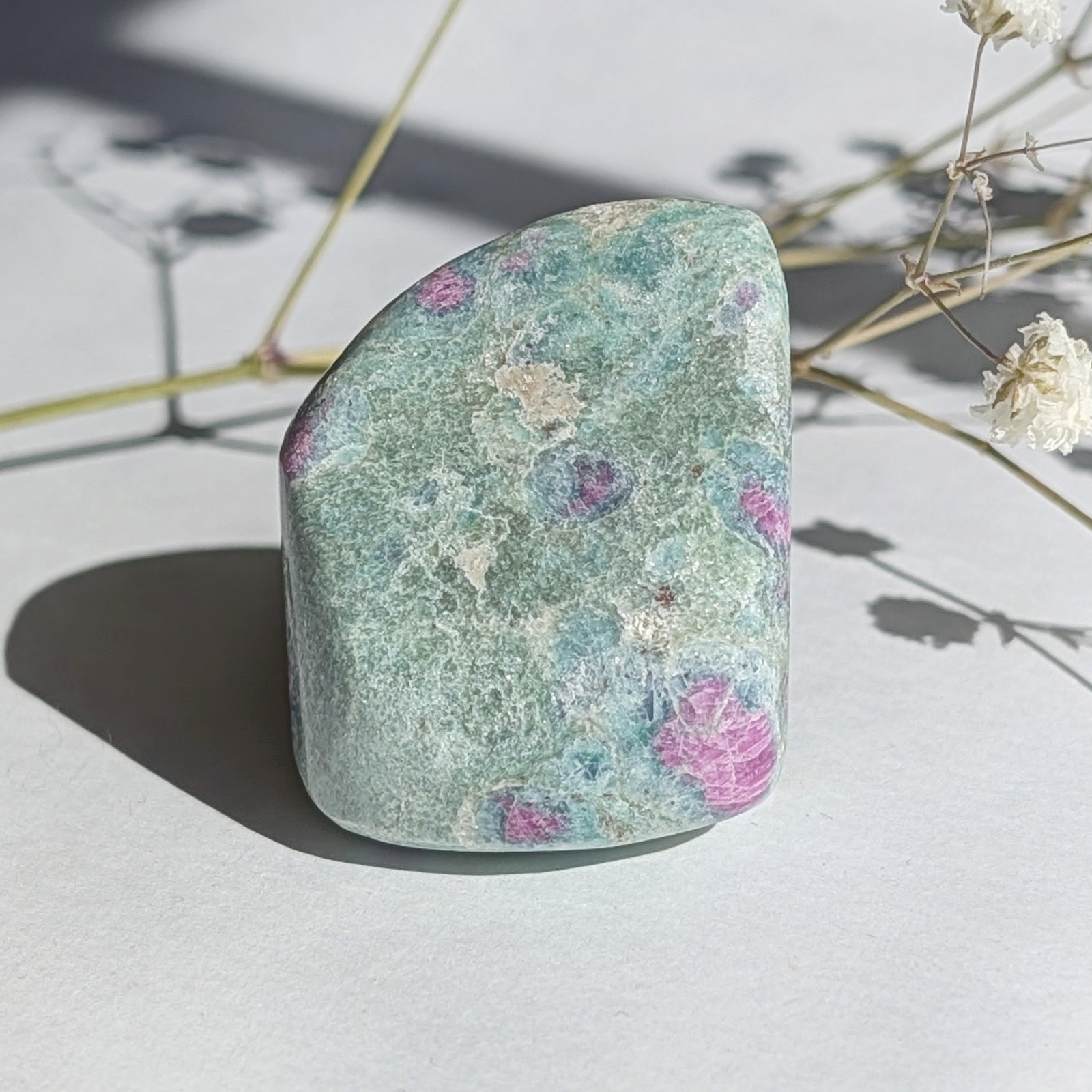 1.5″ shimmery pastel ruby in fuchsite tumble, self stands, UV reactive crystal