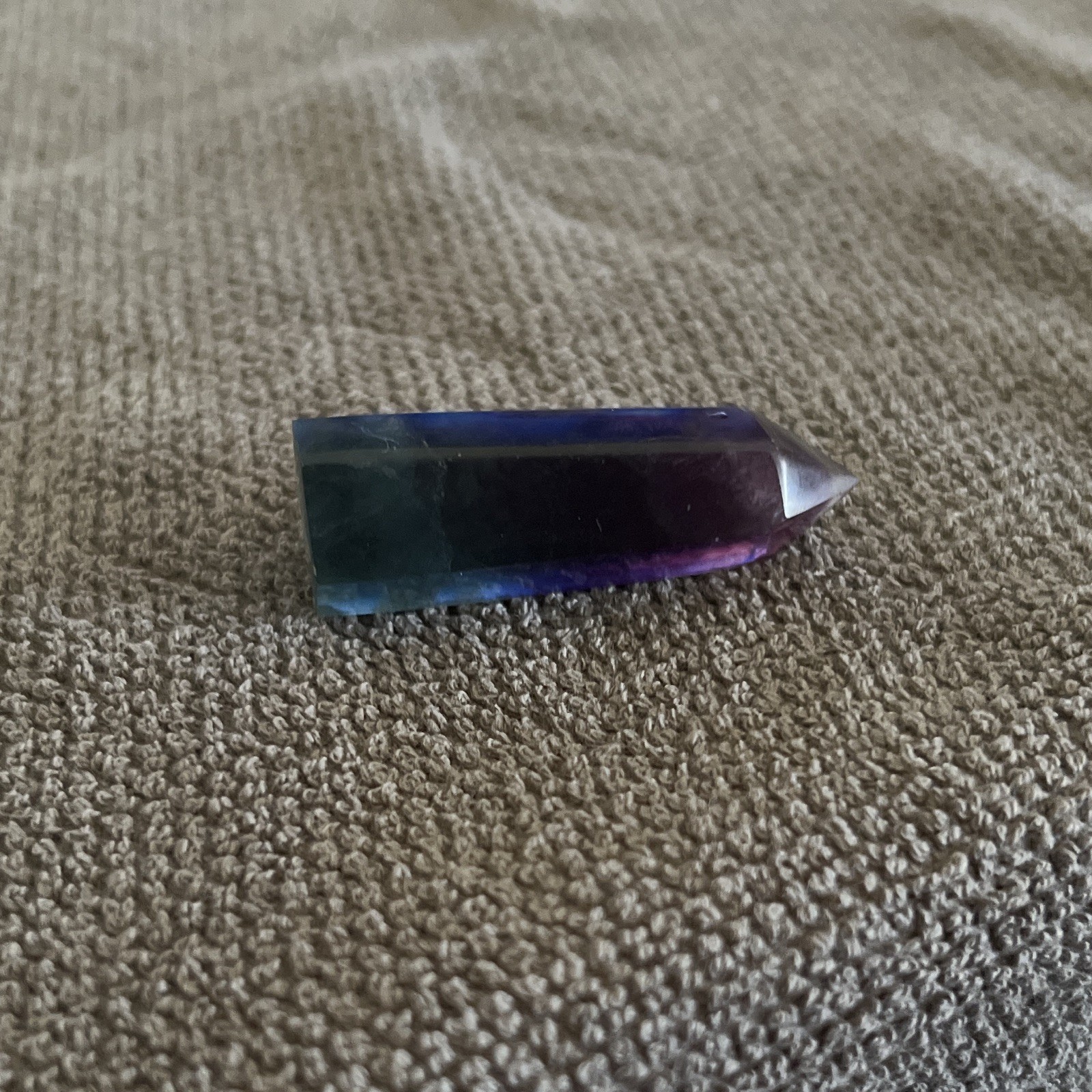 A polished rainbow fluorite crystal wand featuring distinct purple,blue,green